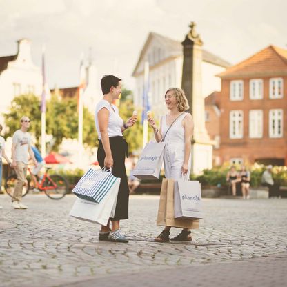 Zwei Frauen essen ein Eis mit Einkaufstaschen auf dem Eutiner Marktplatz