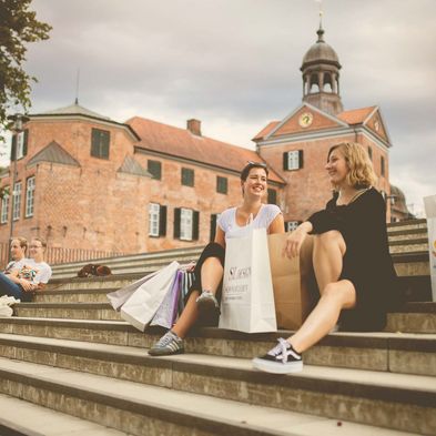 Menschen sitzen auf der Treppe beim Schloss Eutin mit Einkaufstaschen neben sich