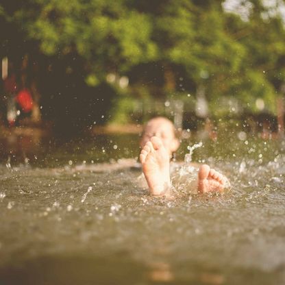 Eine Mädchen schwimmt auf dem Rücken, ihre Füße ragen aus dem Wasser.