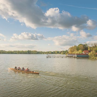 Ruderer fahren auf dem Großen Eutiner See, vorbei an der historischen Badeanstalt