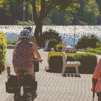 Radfahrer fahren auf den in der Sonne glitzernden Dieksee zu. 