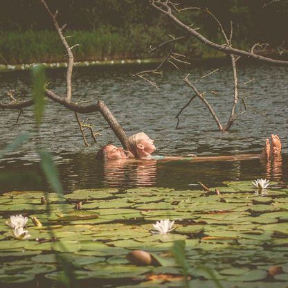 Vater und Tochter schwimmen im See, Seerosen sind im Vordergrund