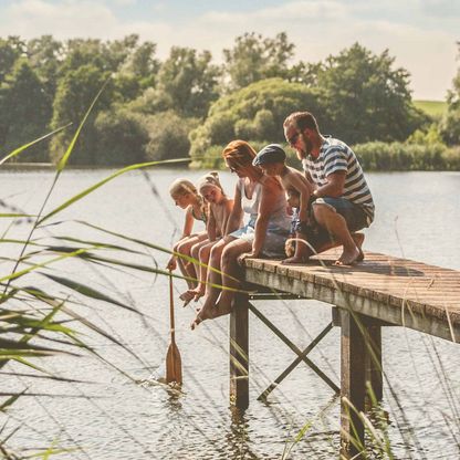 Eine Familie sitzt auf einem Steg und entspannt an einem See.